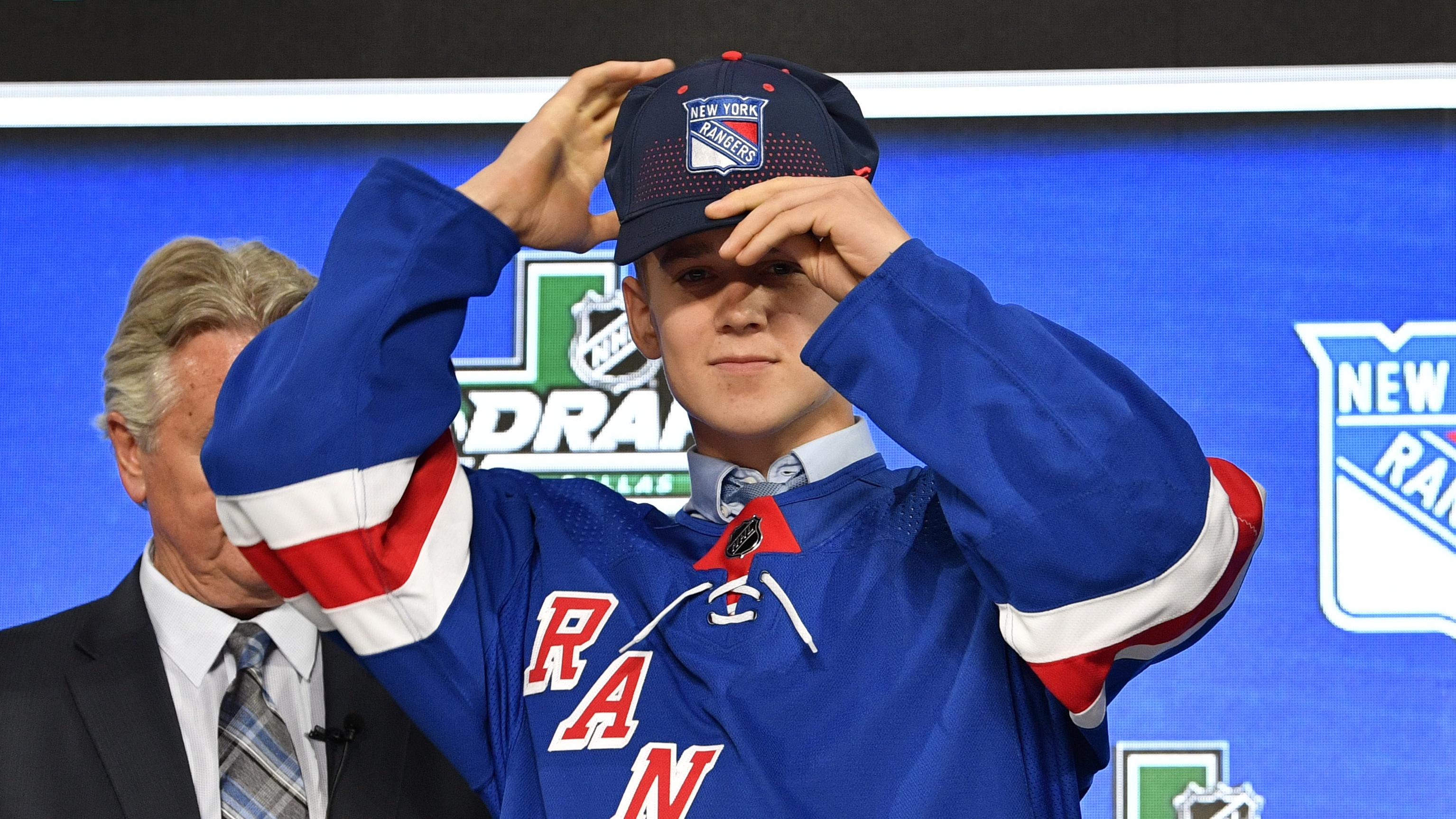 Nils Lundkvist puts on Rangers hat 6/2Jun 22, 2018; Dallas, TX, USA; Nils Lundkvist puts on a team cap after being selected as the number twenty-eight overall pick to the New York Rangers in the first round of the 2018 NHL / © Jerome Miron-USA TODAY Sports